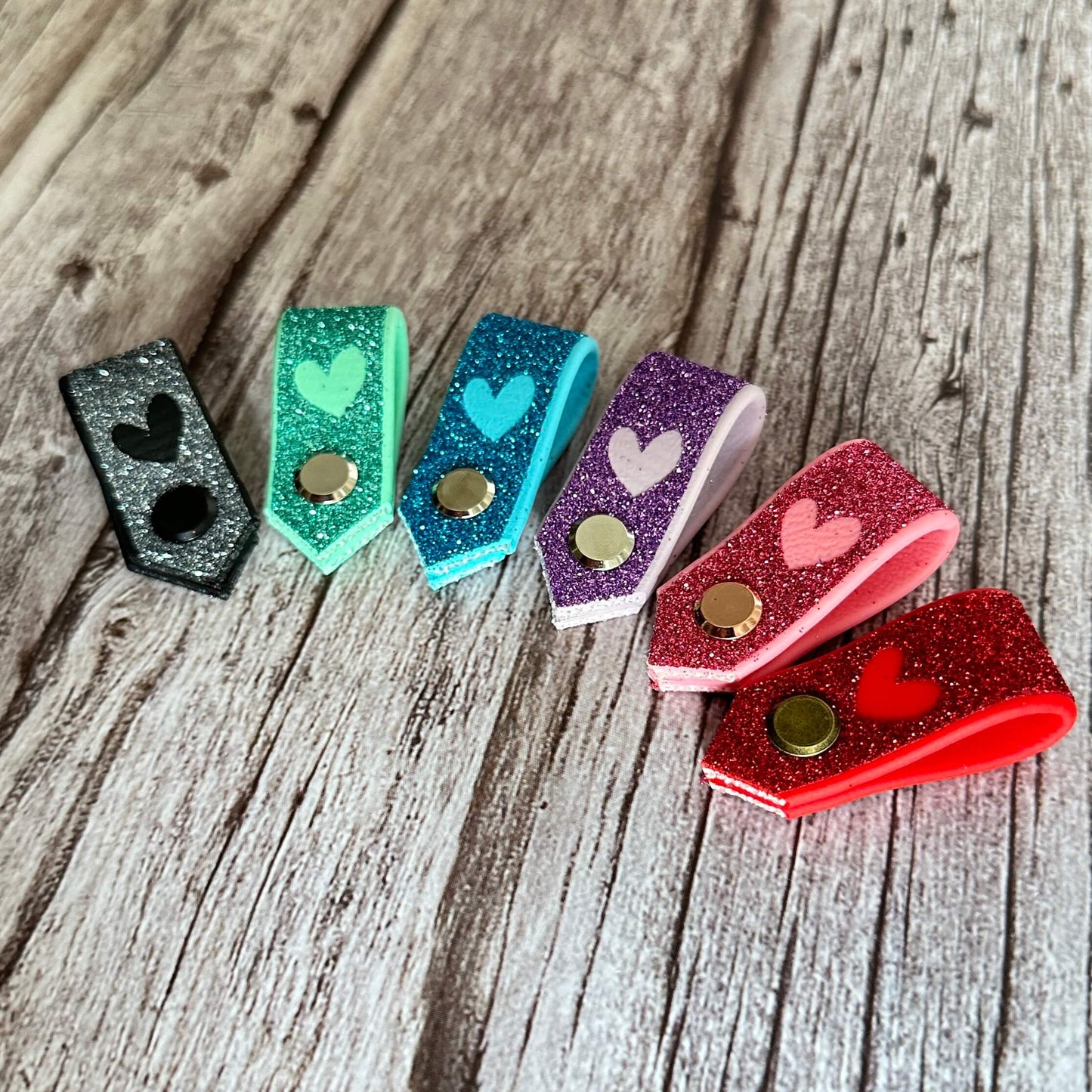 Sechs glitzernde Druckknöpfe in Schwarz, Grün, Blau, Lila, Weiß und Rosa mit Herzmotiven von StallSchätze sind übersichtlich angeordnet - ein niedliches Accessoire für Ihren Glitzer-Halfter-Tag.