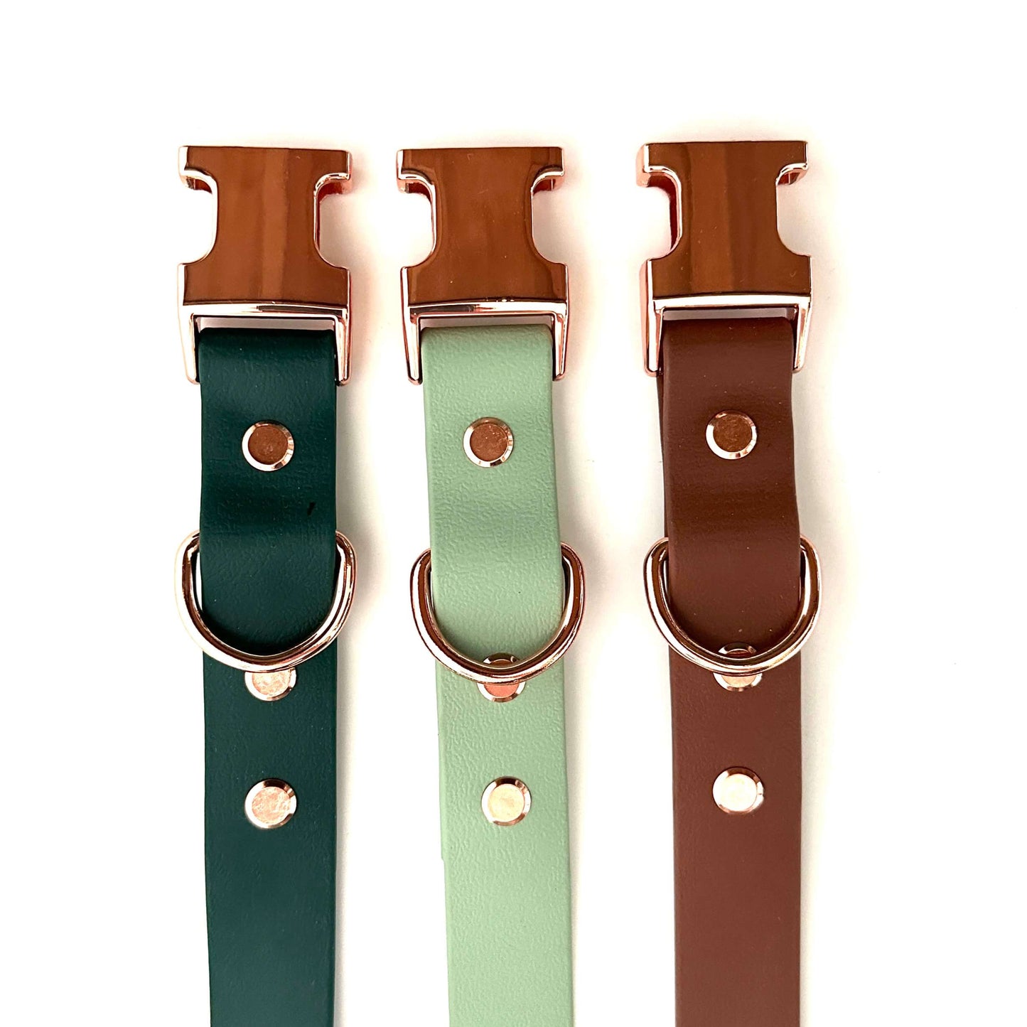 Drei StallSchätze Hundehalsbänder aus Biothane mit roségoldenen Beschlägen in Dunkelgrün, Mintgrün und Braun liegen vertikal auf weißem Hintergrund.