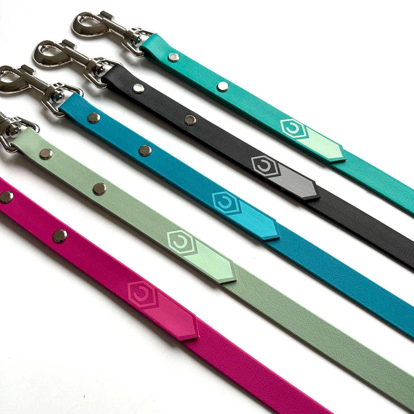Fünf Biothane-Führstrick klassisch Leinen von StallSchätze, jeweils mit einem Sechseck-Logo und schicker Verzierung, sind diagonal auf Weiß abgebildet. Die Leinen mit Metallverschluss gibt es in Pink, Hellgrün, Petrol, Schwarz und Türkis.