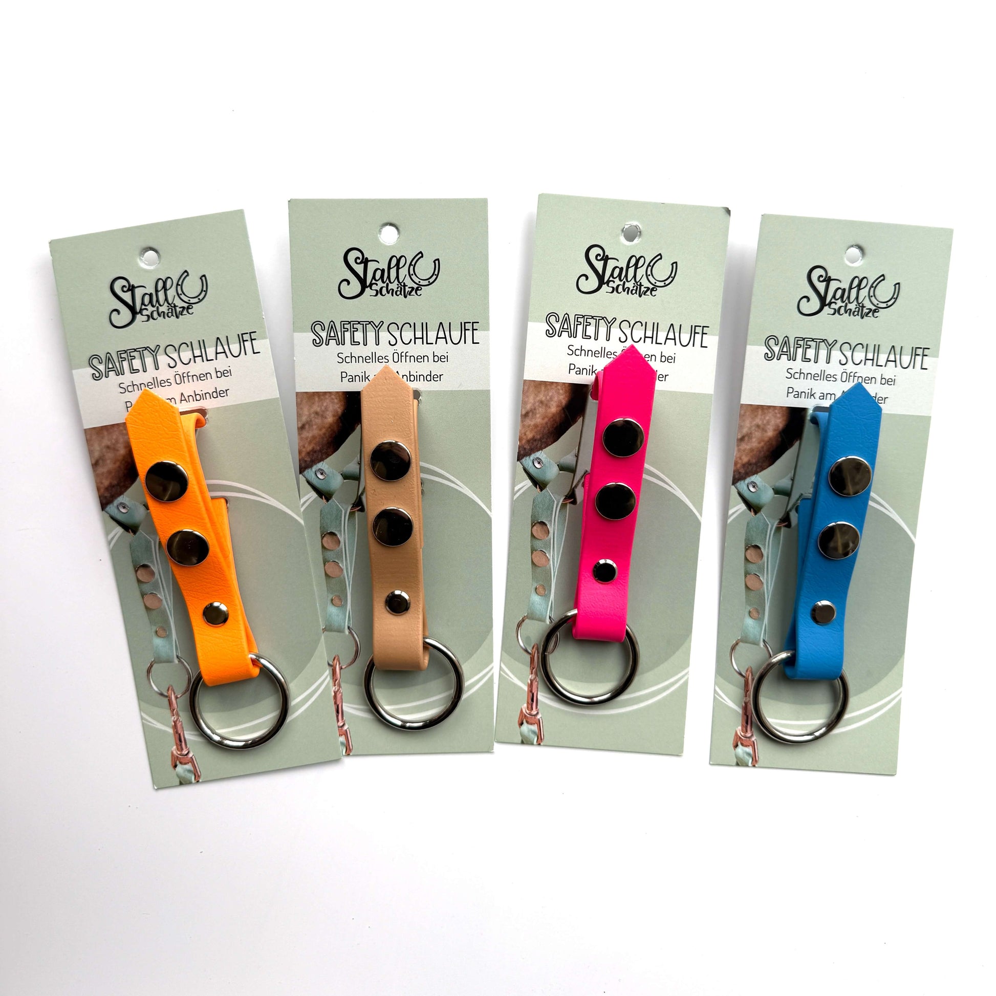 Vier StallSchätze Safety-Schlaufe für Halfter Schlüsselanhänger in Gelb, Hellbraun, Rosa und Blau - jeweils mit Produktkarte und Metallring - stehen nebeneinander auf weißem Grund, perfekt für Pferdefans.