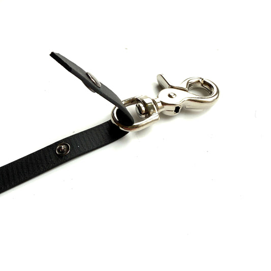 Eine Nahaufnahme der schwarzen StallSchätze Safety-Schweifriemen mit Sollbruch-Stelle mit silbernem Drehverschluss und Druckknopf, dargestellt vor weißem Hintergrund.
