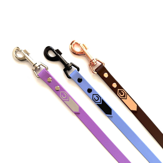 Drei Führstrick für den HalfterSchatz Hundeleinen von StallSchätze - lila, hellblaue und braune Bänder mit silbernen, schwarzen und roségoldenen Bolzenkarabinern - sind nebeneinander auf weißem Hintergrund angeordnet.