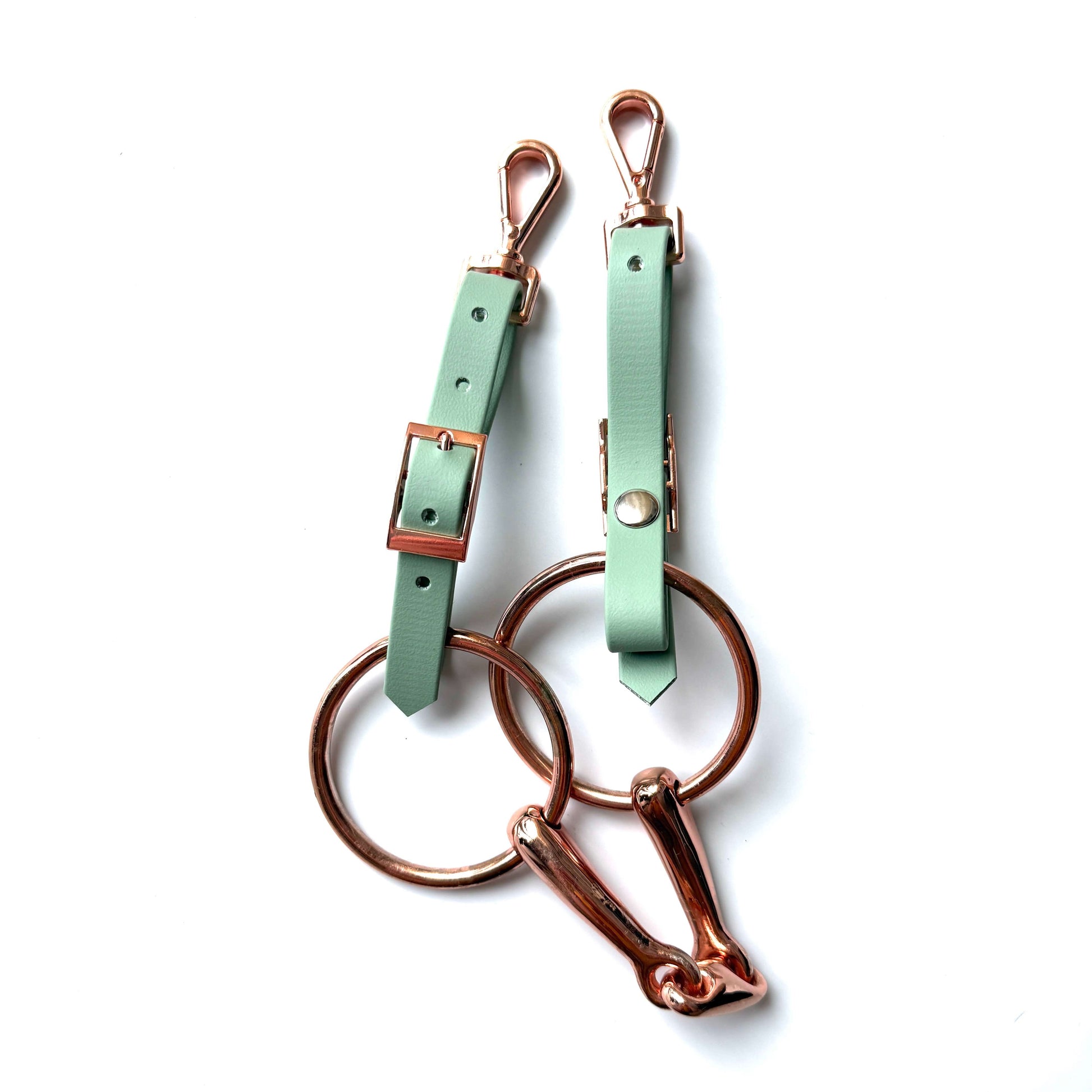 Zwei mintgrüne StallSchätze Edle Biothane-Bithanger mit goldenen Schnallen, Verschlüssen und großen Ringen sind auf weißem Hintergrund abgebildet; ein Ring ist zusätzlich mit einem goldenen Karabinerhaken versehen.