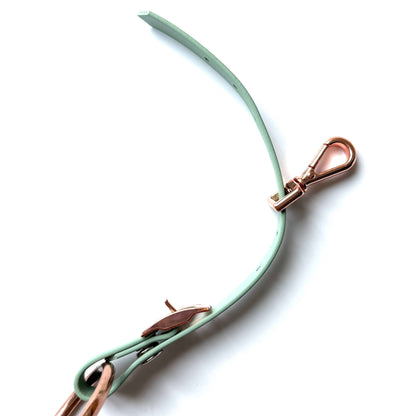 Der StallSchätze Edle Biothane-Bithanger mit Schnappkarabiner hat ein blassgrünes Armband mit roségoldener Schließe und Dornschließe, abgebildet vor einem weißen Hintergrund.